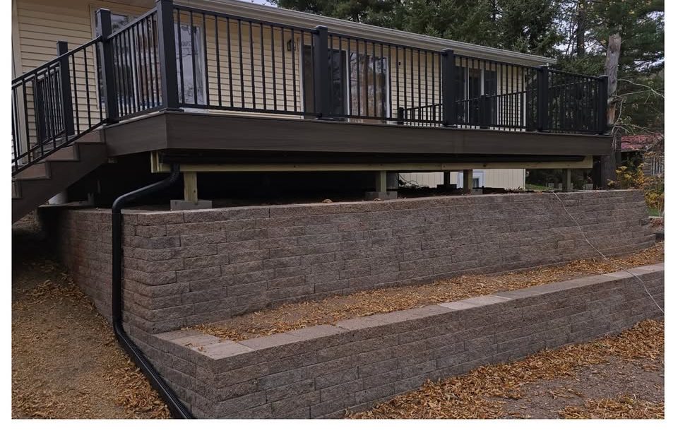 A finished composite deck with black railings above a new block retaining wall, built by T&A Contracting