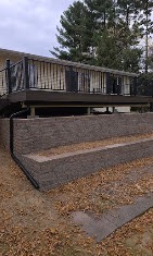 Elevated deck with black railing above a gray block retaining wall by T & A Contracting
