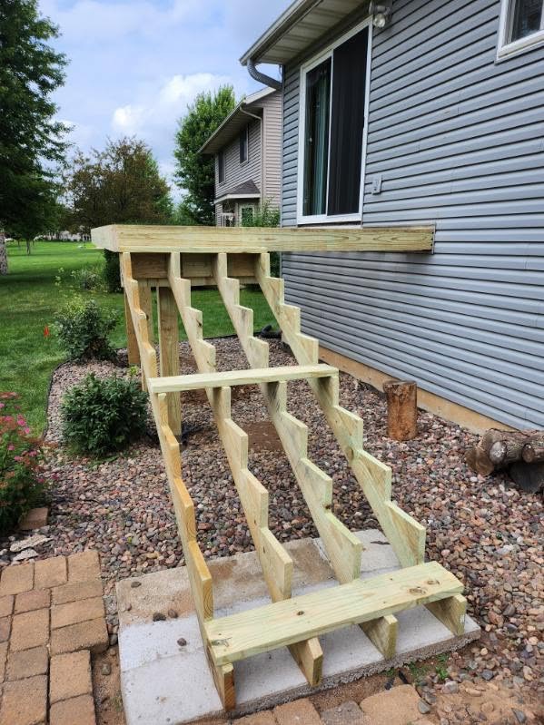 Freshly cut pressure-treated deck stair stringers on a concrete pad by T & A Contracting