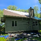Green-stained cabin with a new teal standing-seam metal roof by T & A Contracting